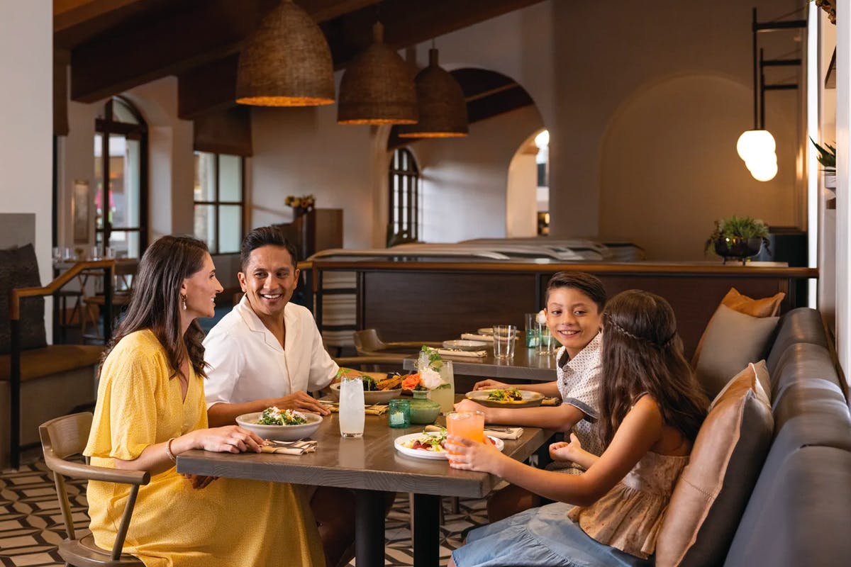Family of four enjoying a dinner inside Zachari Dunes destination property by Hilton