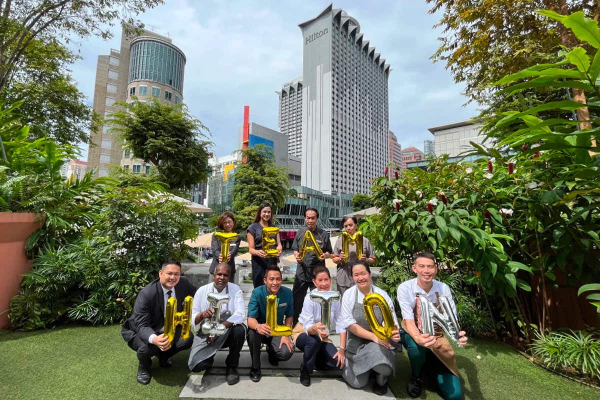 Employees holding balloon letters that read "team Hilton" in front of a hilton hotel in Singapore