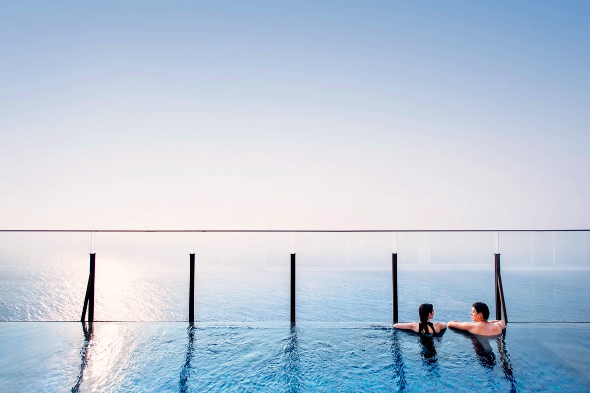 Two people swimming in a infinity pool while looking at the sun rise