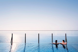 Two people swimming in a infinity pool while looking at the sun rise