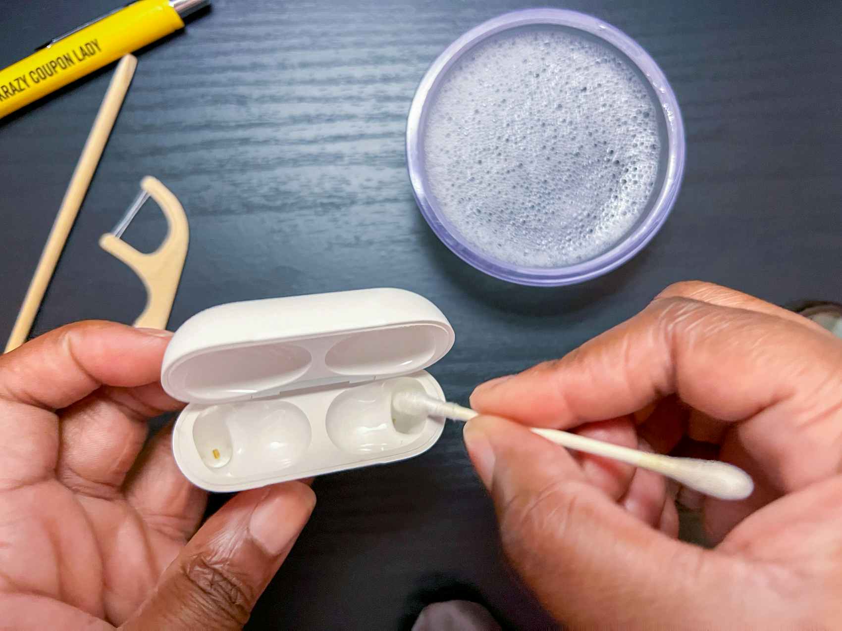 Person using a cotton swab to clean hard to reach areas inside an airpod case
