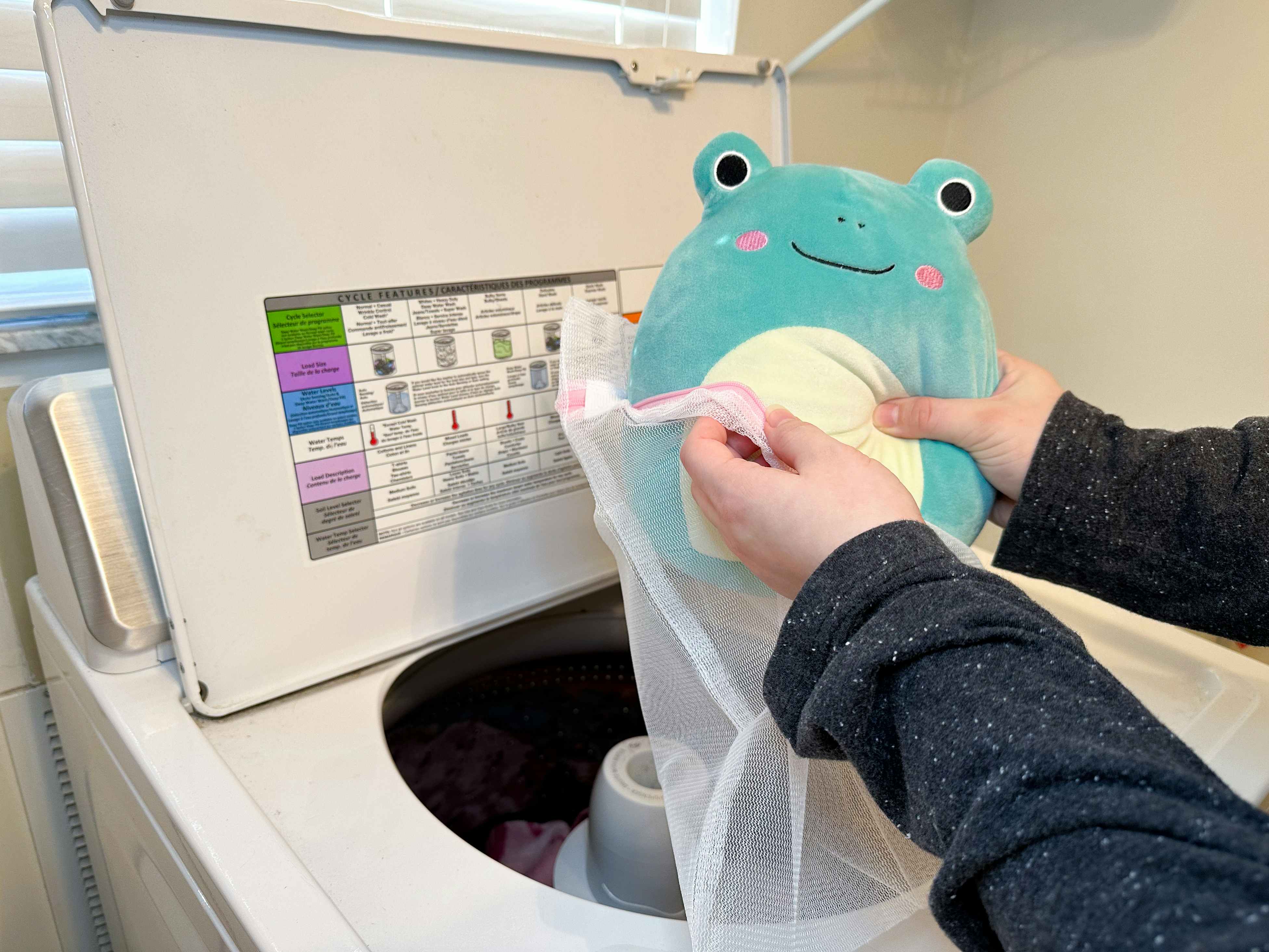 Someone putting a Squishmallow into a mesh bag above the washing machine