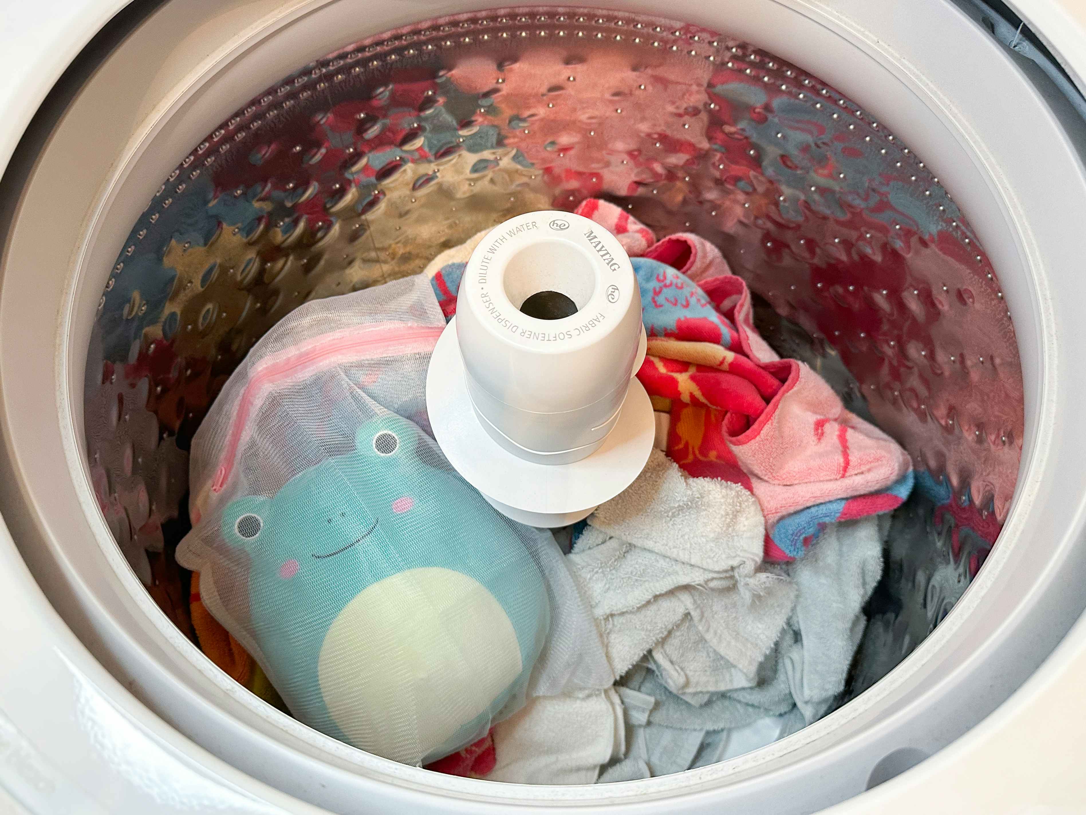 A Squishmallow in a mesh bag in a washing machine with towels