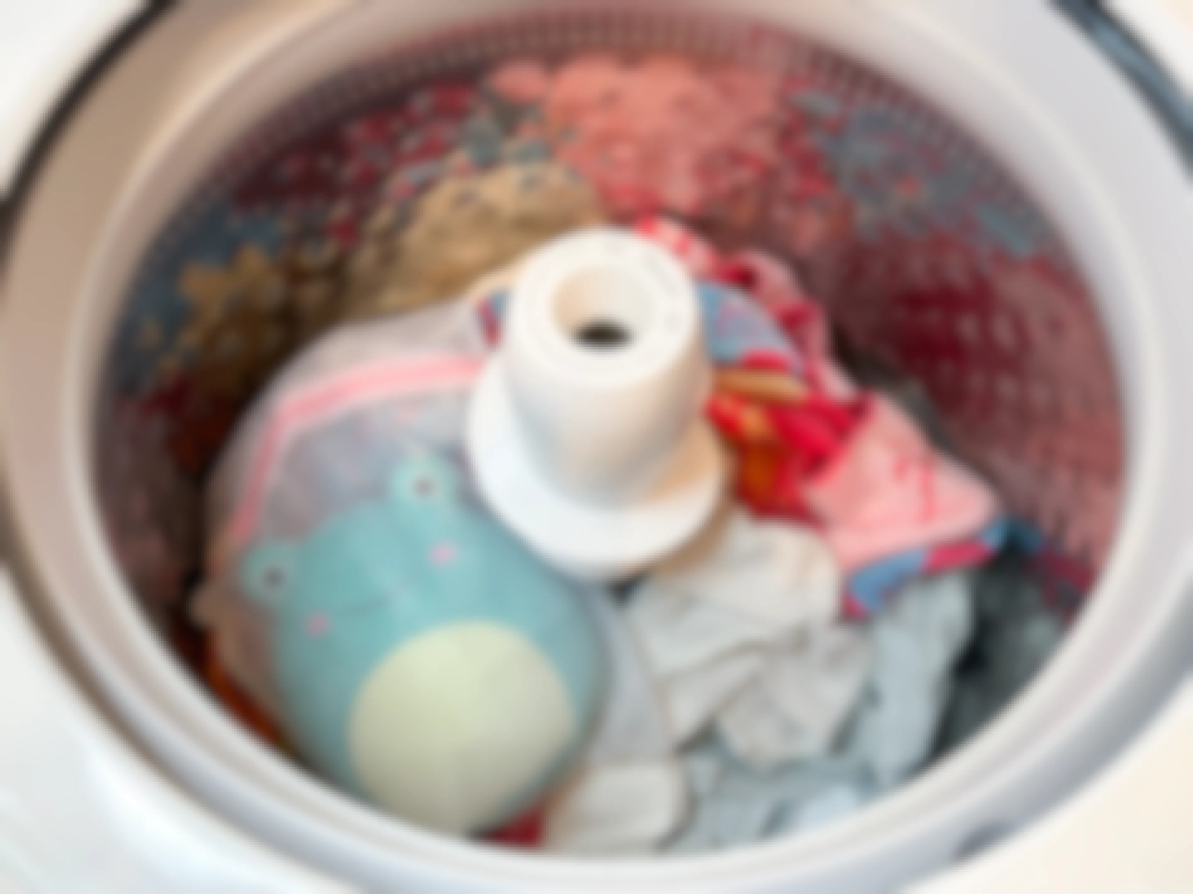 A Squishmallow in a mesh bag in a washing machine with towels