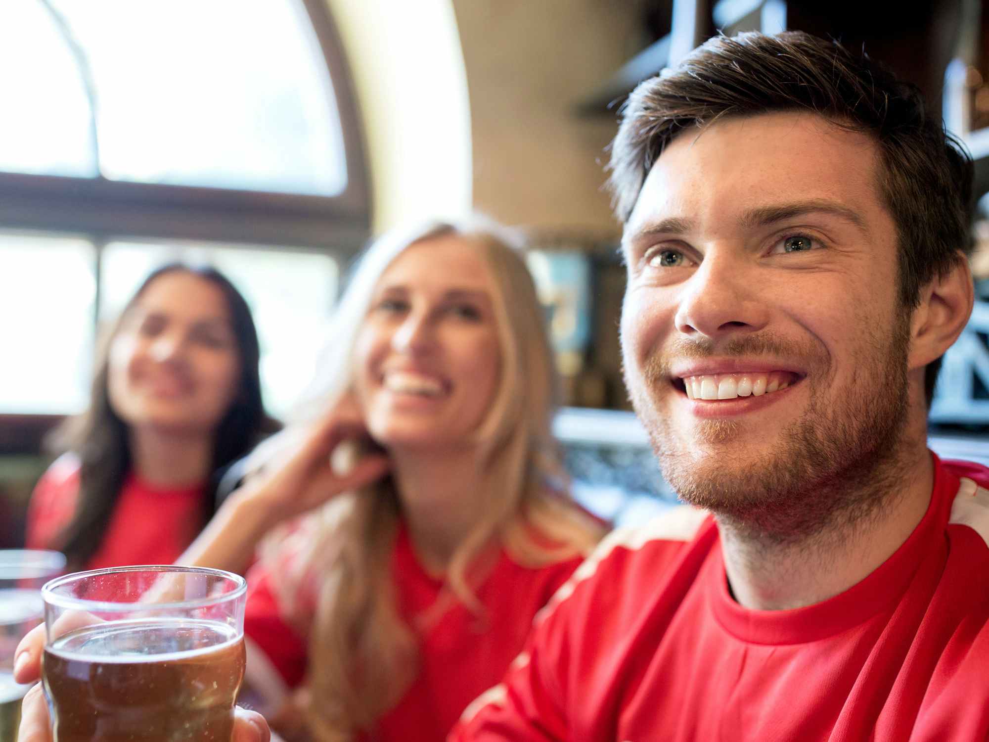 friends in red drinking beer and watching game at bar