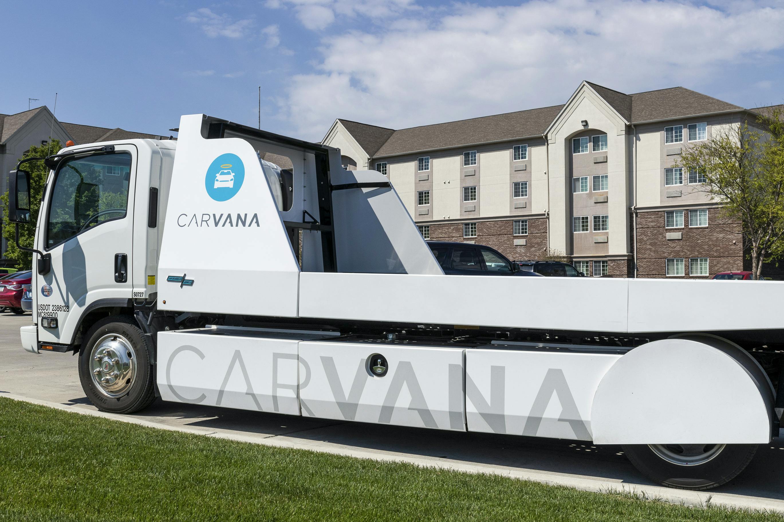 A Carvana truck parked outside of a house, ready to pick up a vehicle