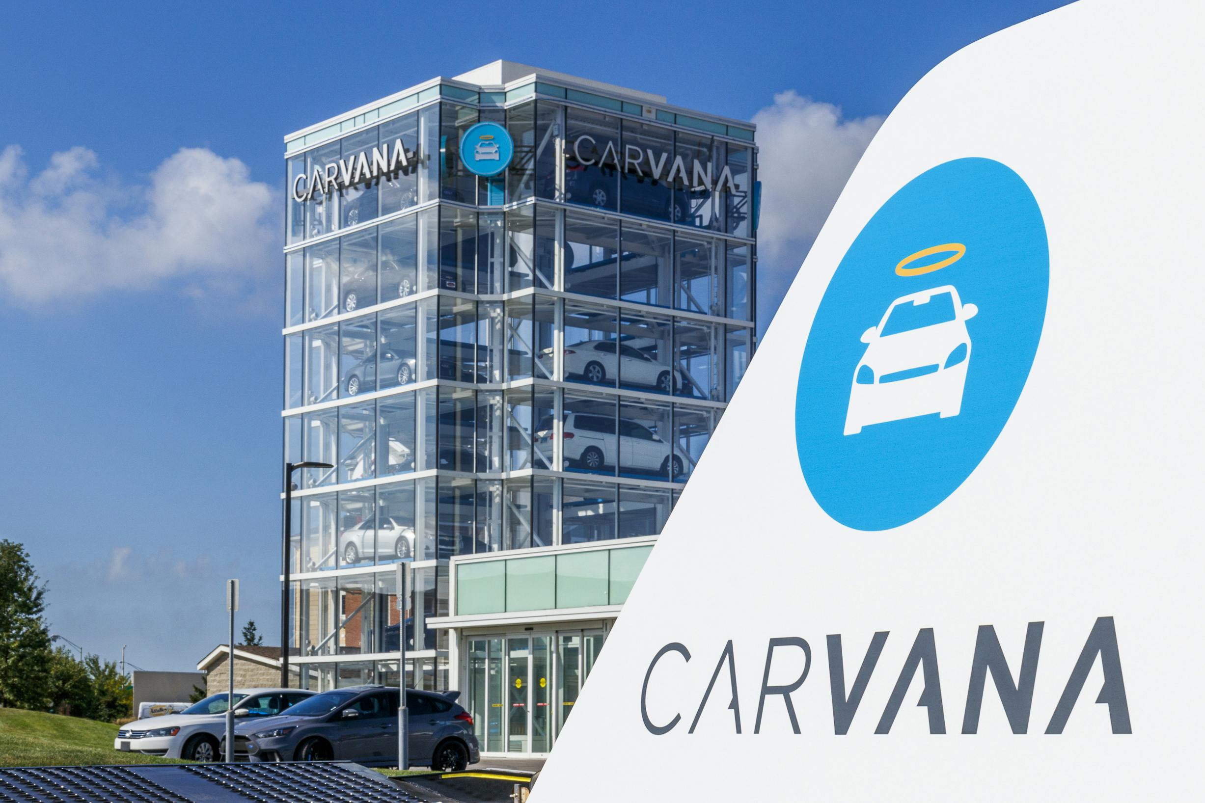 A Carvana sign with the Carvana building in the background with vehicles parked in front of it