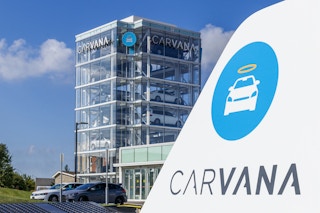 A Carvana sign with the Carvana building in the background with vehicles parked in front of it