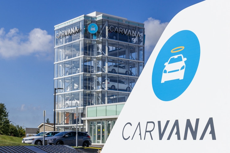 A Carvana sign with the Carvana building in the background with vehicles parked in front of it