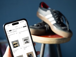 Someone looking at sneakers on the GOAT app with sneakers in the background