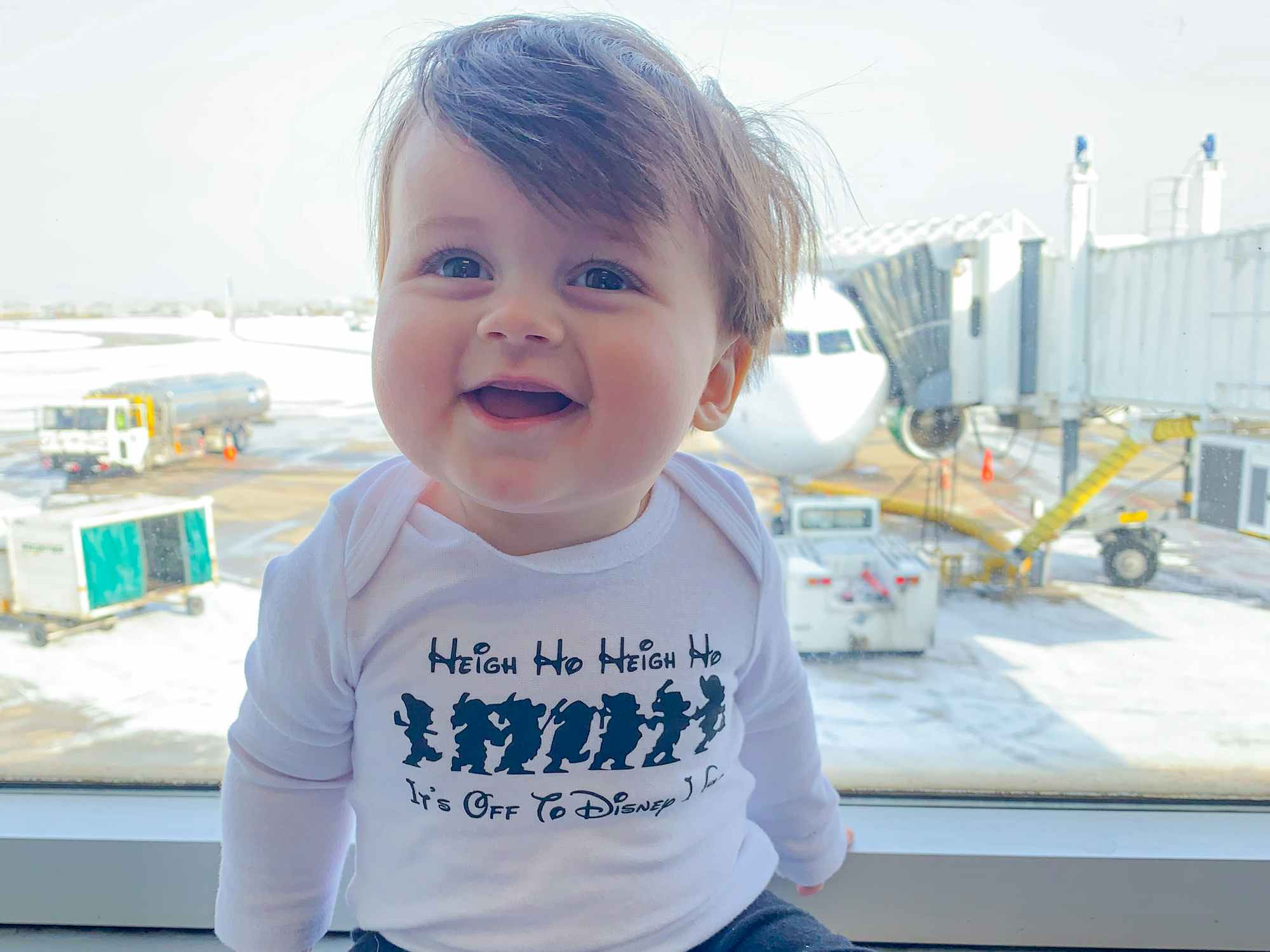 a baby sitting by a window at an airport with an airplane in the background