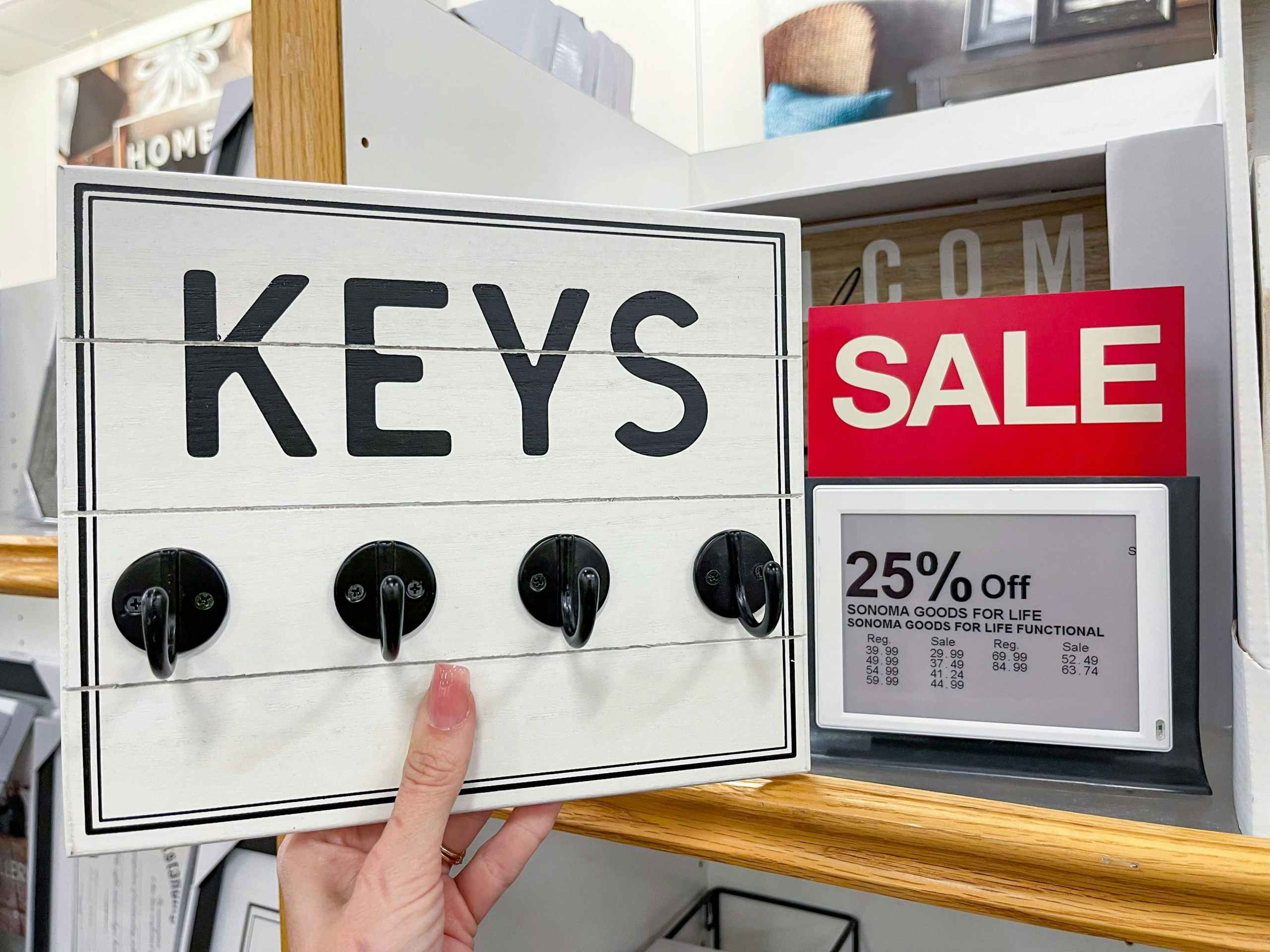 somone holding up wall decor with hooks that says keys
