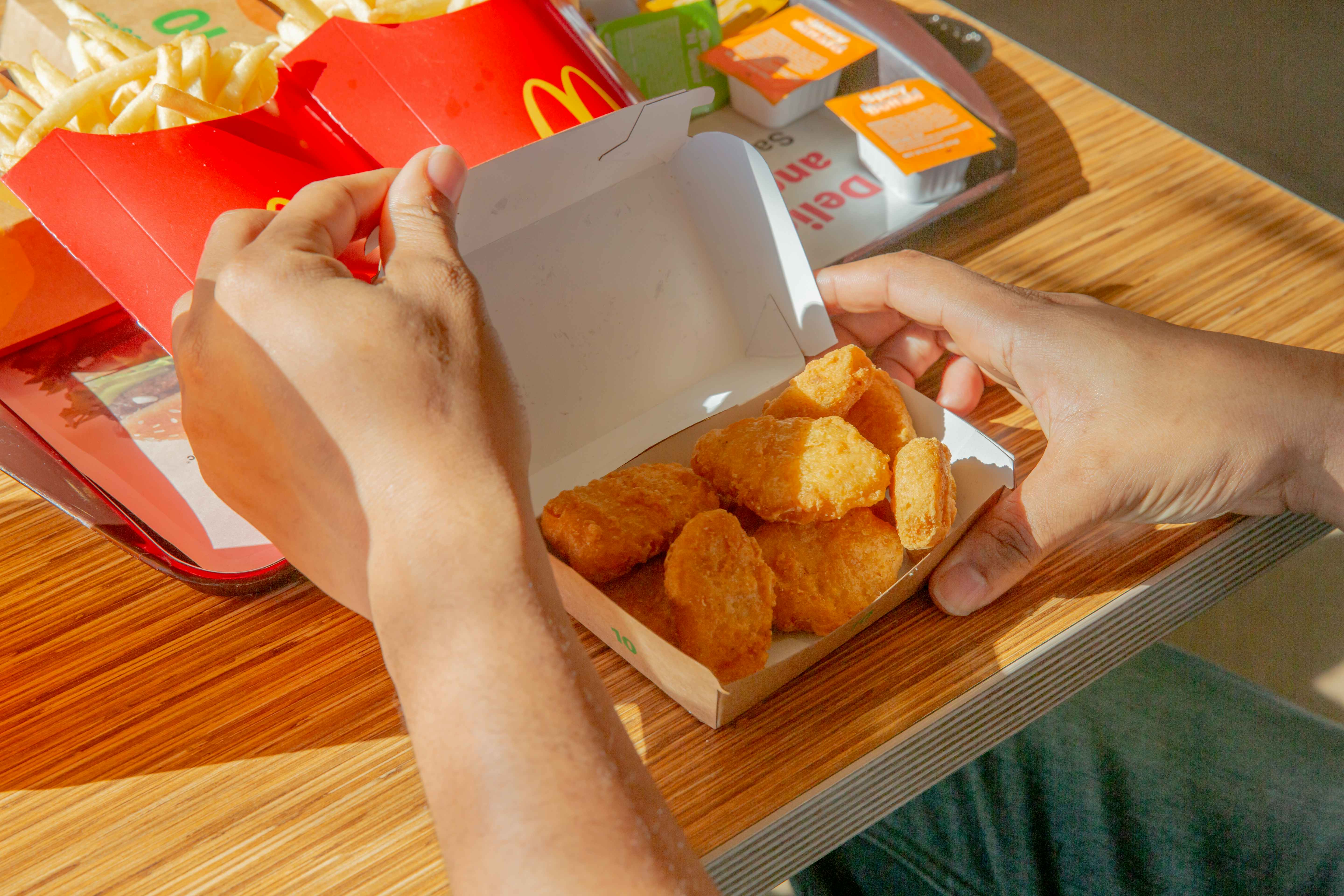 Person opening a box of chicken nuggets from McDonalds with buffalo sauce in the background
