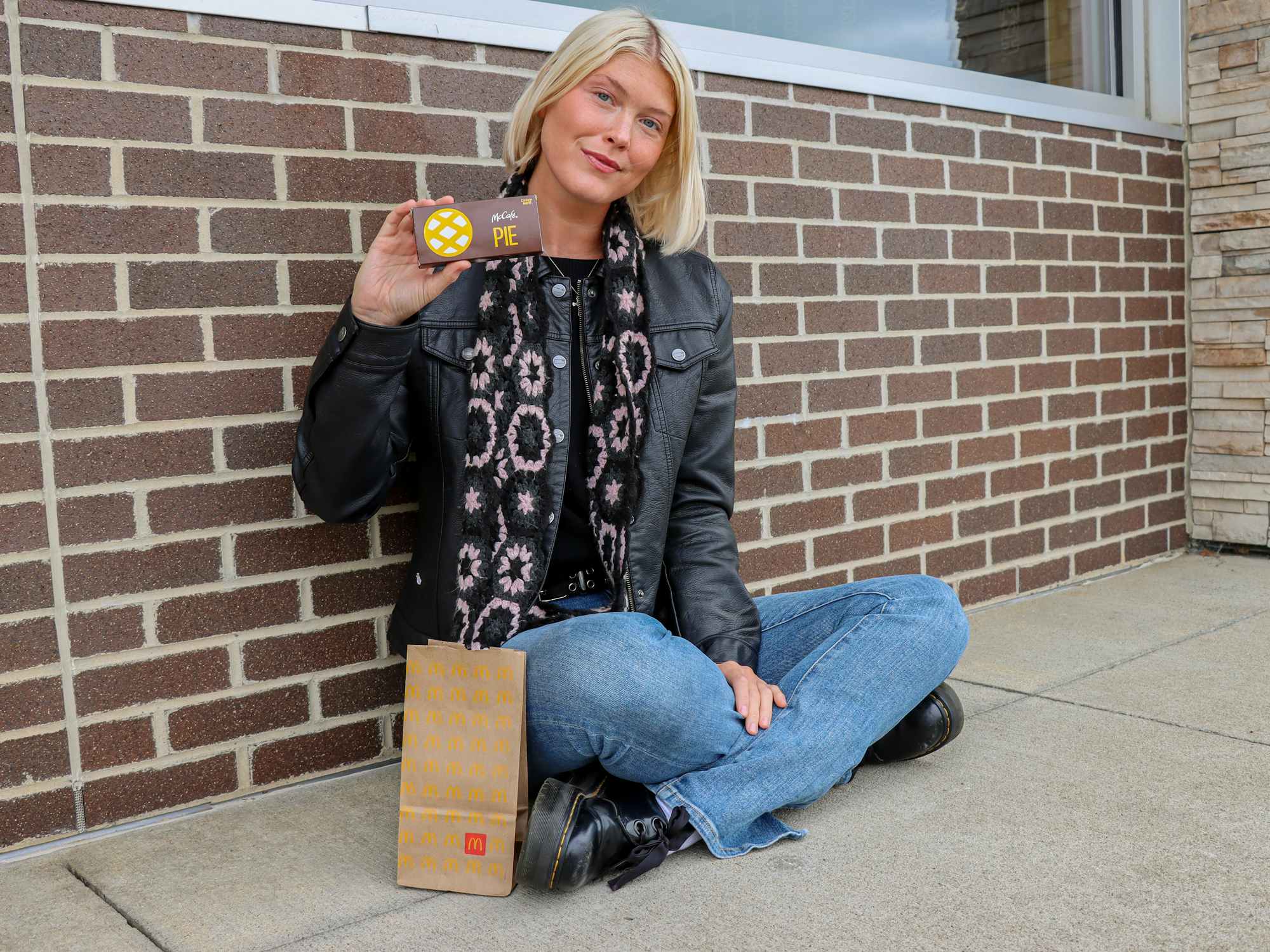 a person sitting outside of mcdonalds holding up a pie