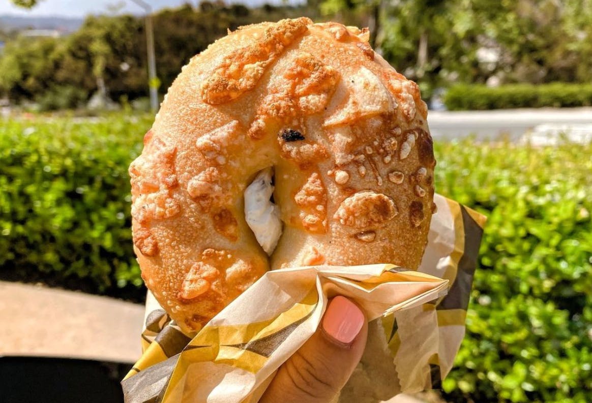 person holding up a bagel with cream cheese from einstein bros 