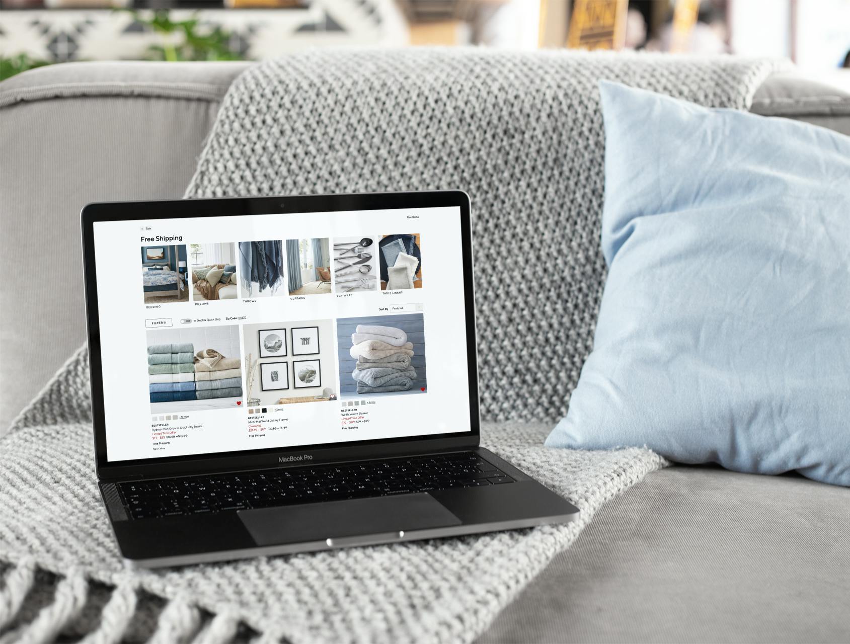 An open laptop sitting by itself on a gray sofa, showing the Pottery Barn free shipping page on its screen