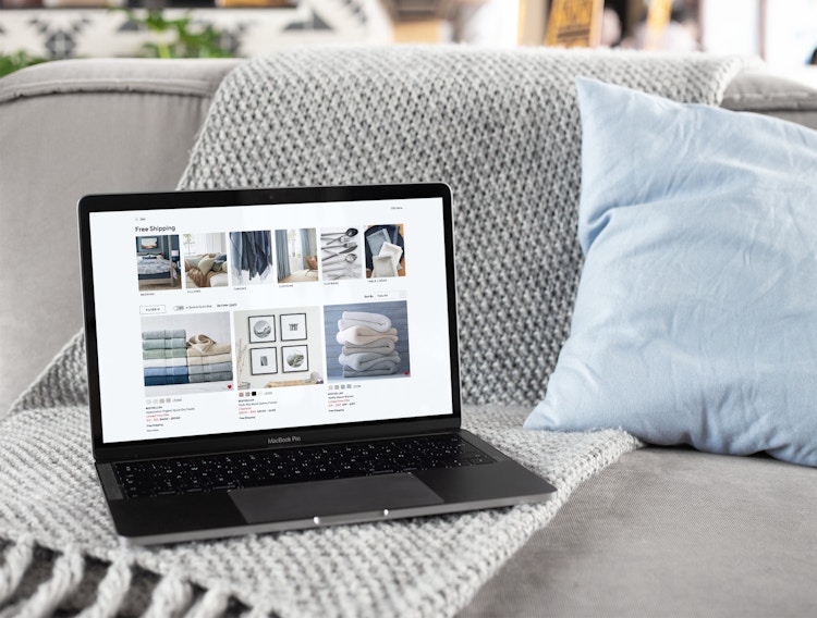 An open laptop sitting by itself on a gray sofa, showing the Pottery Barn free shipping page on its screen