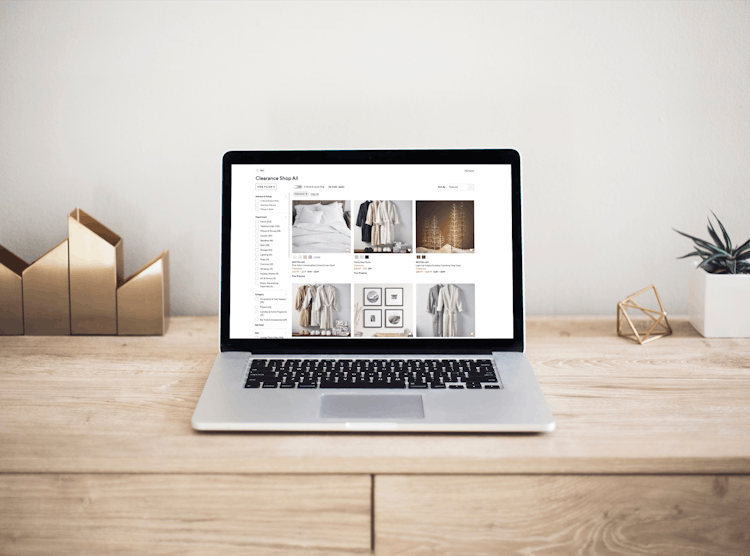 A laptop sitting on a wooden desk open to the clearance page on PotteryBarn.com