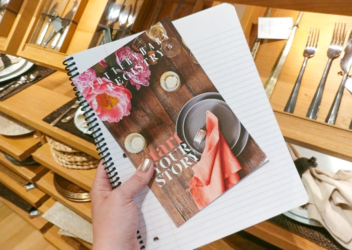 A woman's hand holding a pottery barn registry pamphlet while shopping in the pottery barn store