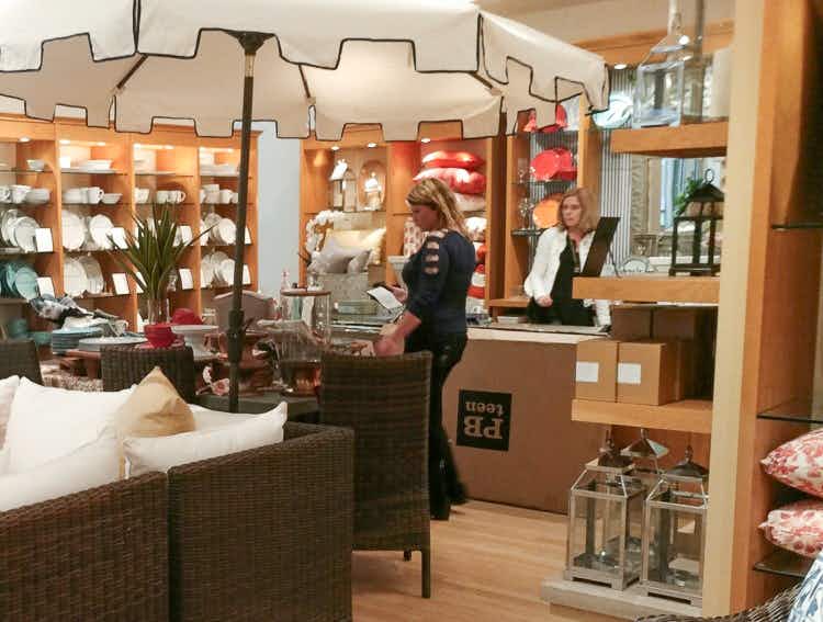 A woman shopping in a Pottery Barn store with a Pottery Barn employee at the checkout counter behind her