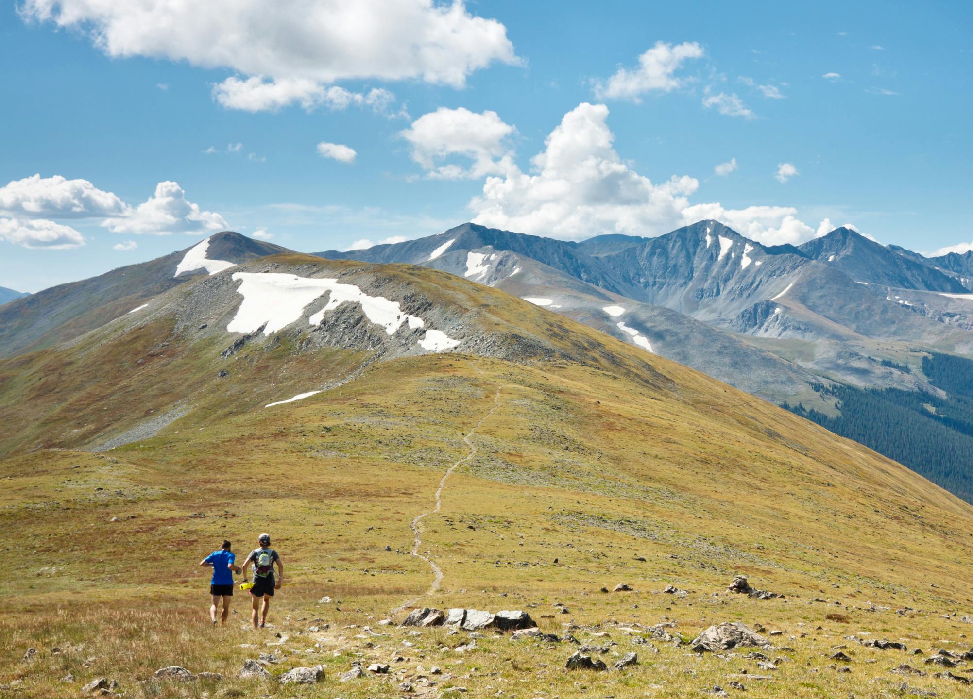 A scenic mountain view of the Rocky Mountains National Park with two hikers walking on a trail along the mountain ridge