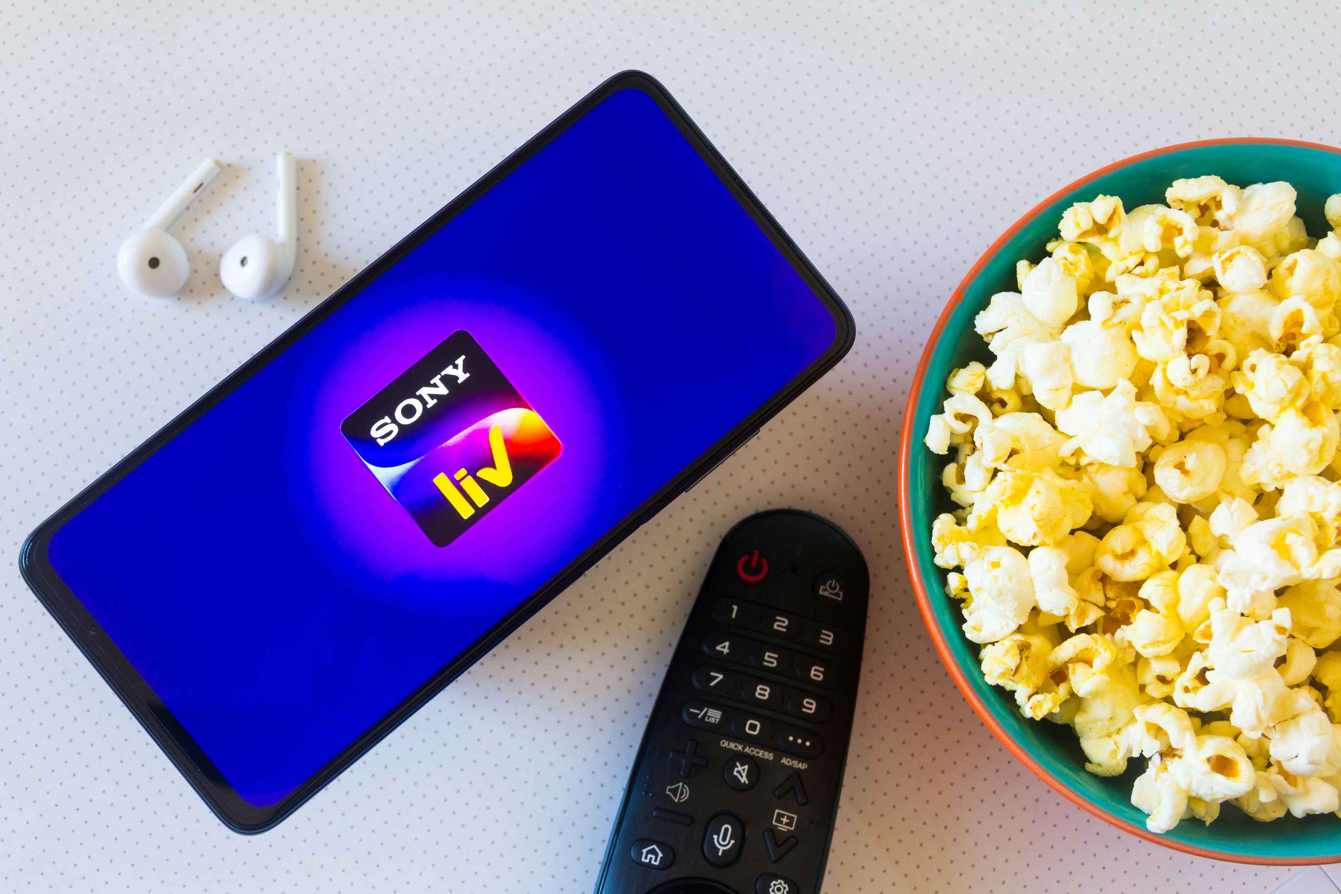 Phone showing the SonyLiv App next to a pair of airpods, a bowl of popcorn and a tv remote.
