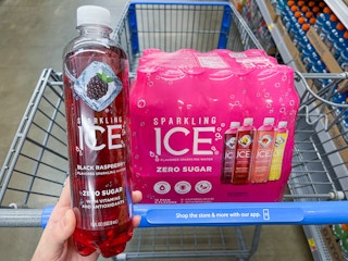 A Sparkling Ice Black Raspberry held out by hand in front of a Sparkling Ice variety package sitting in a store cart.