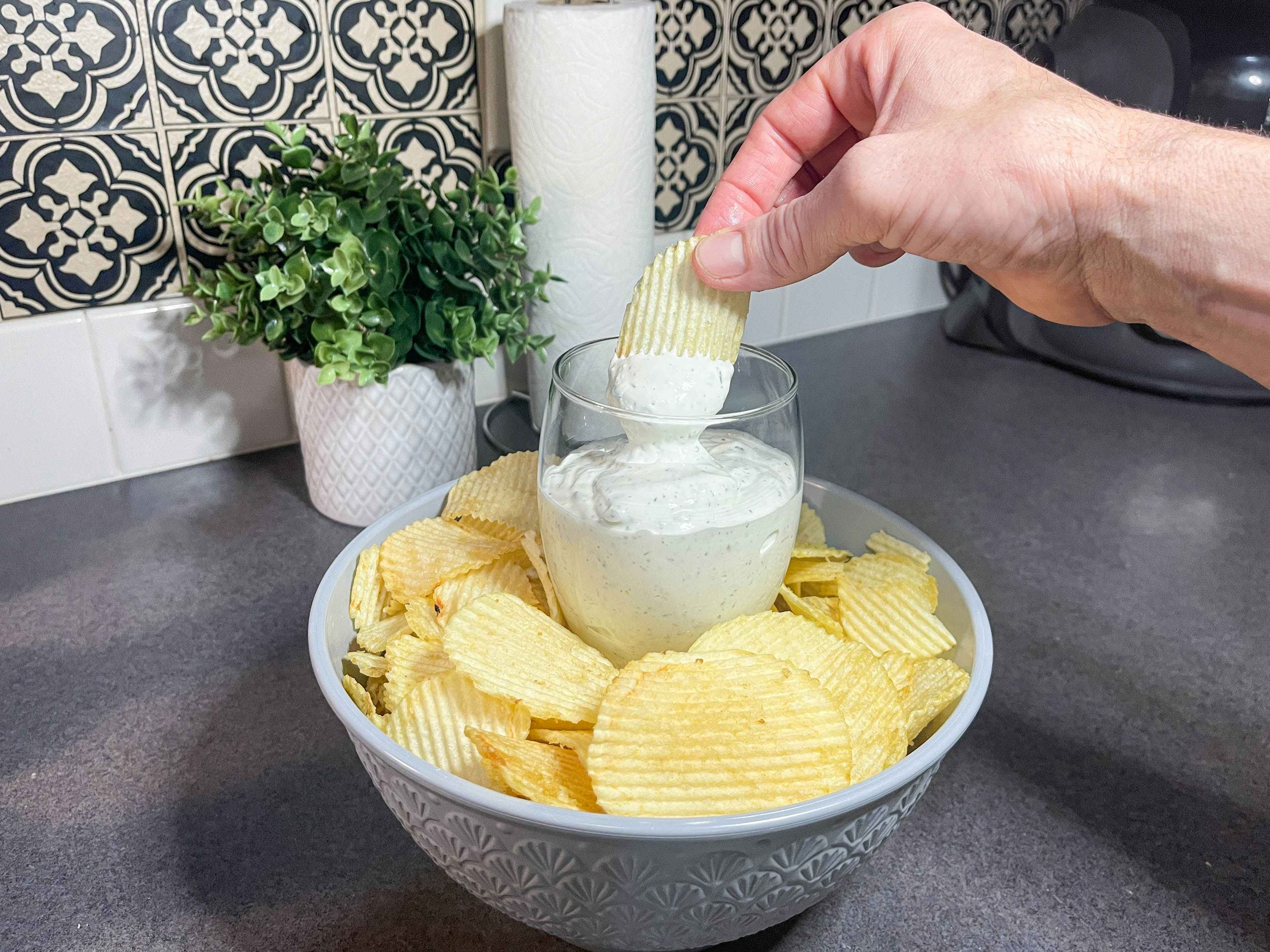 a hand dipping a chip into ranch dip from a wine glass filled with dip 