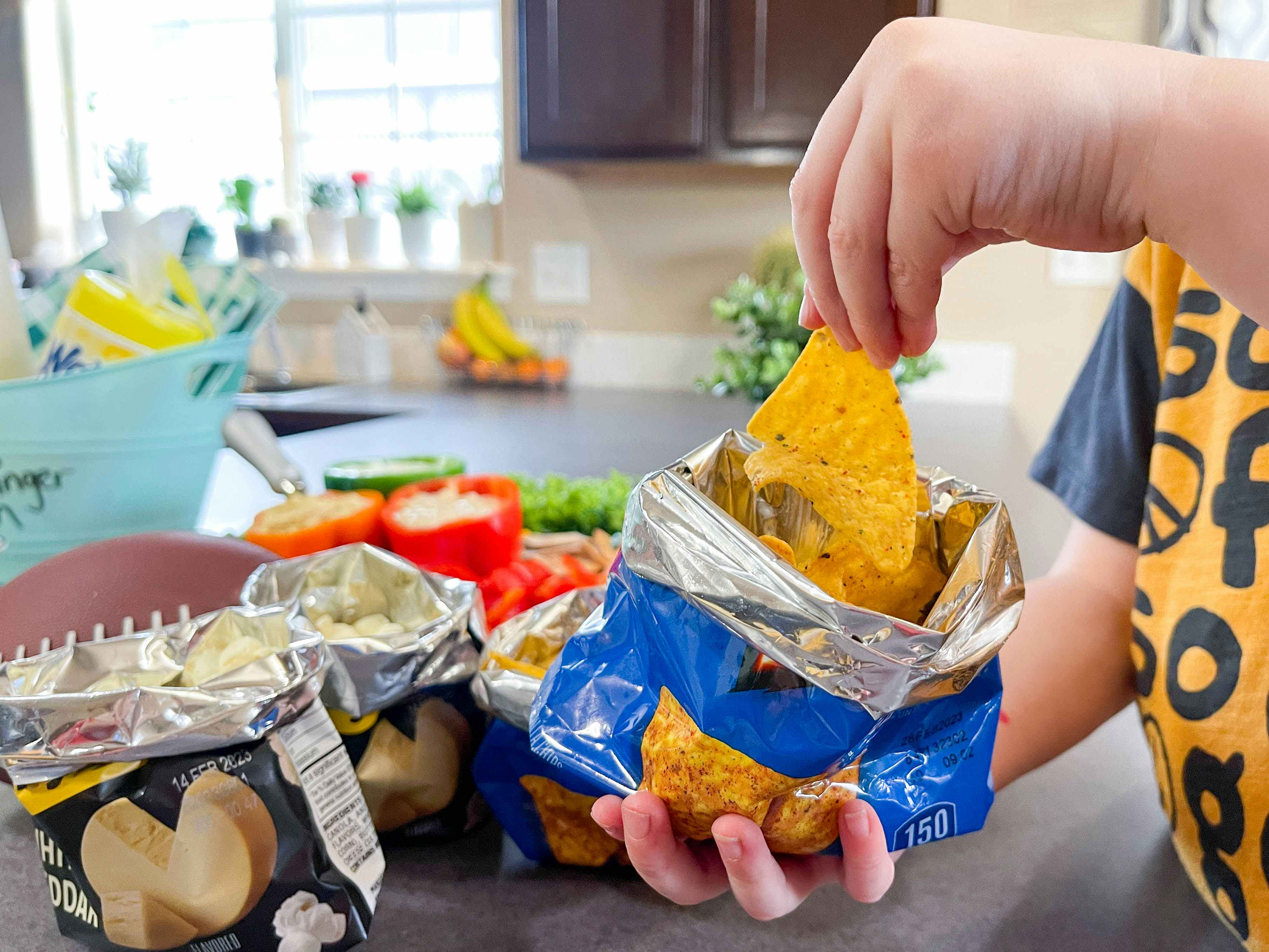 a child's hand grabbing a a chip from a bag of chips 