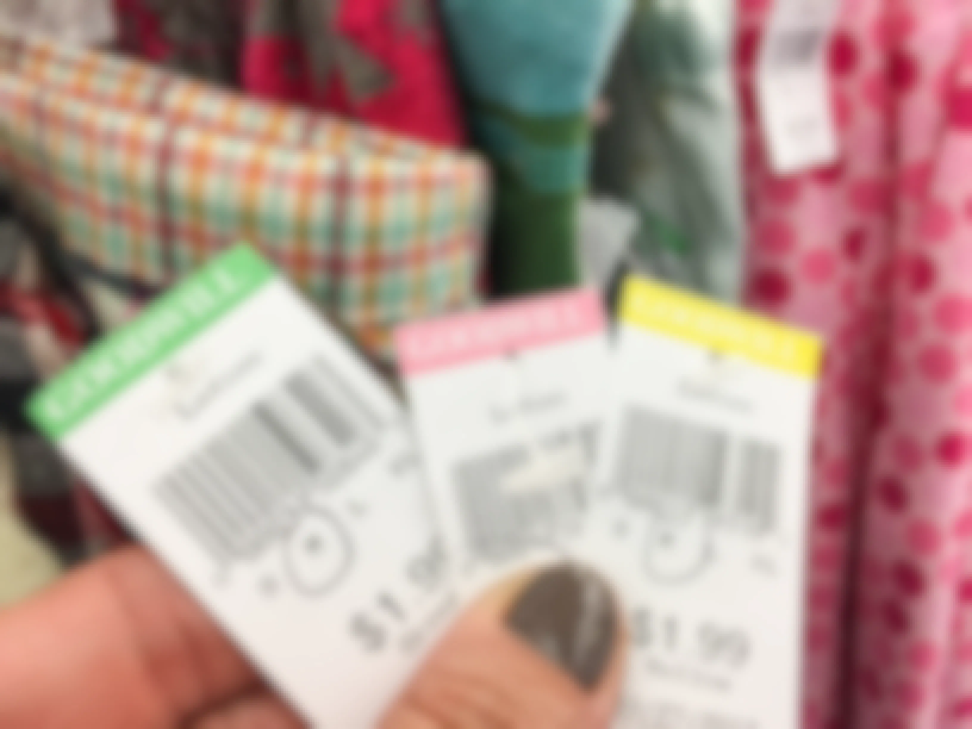 Someone holding up different colored Goodwill price tags in front of a rack of clothing
