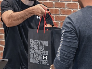 An Under Armour employee handing a shopping bag to a customer