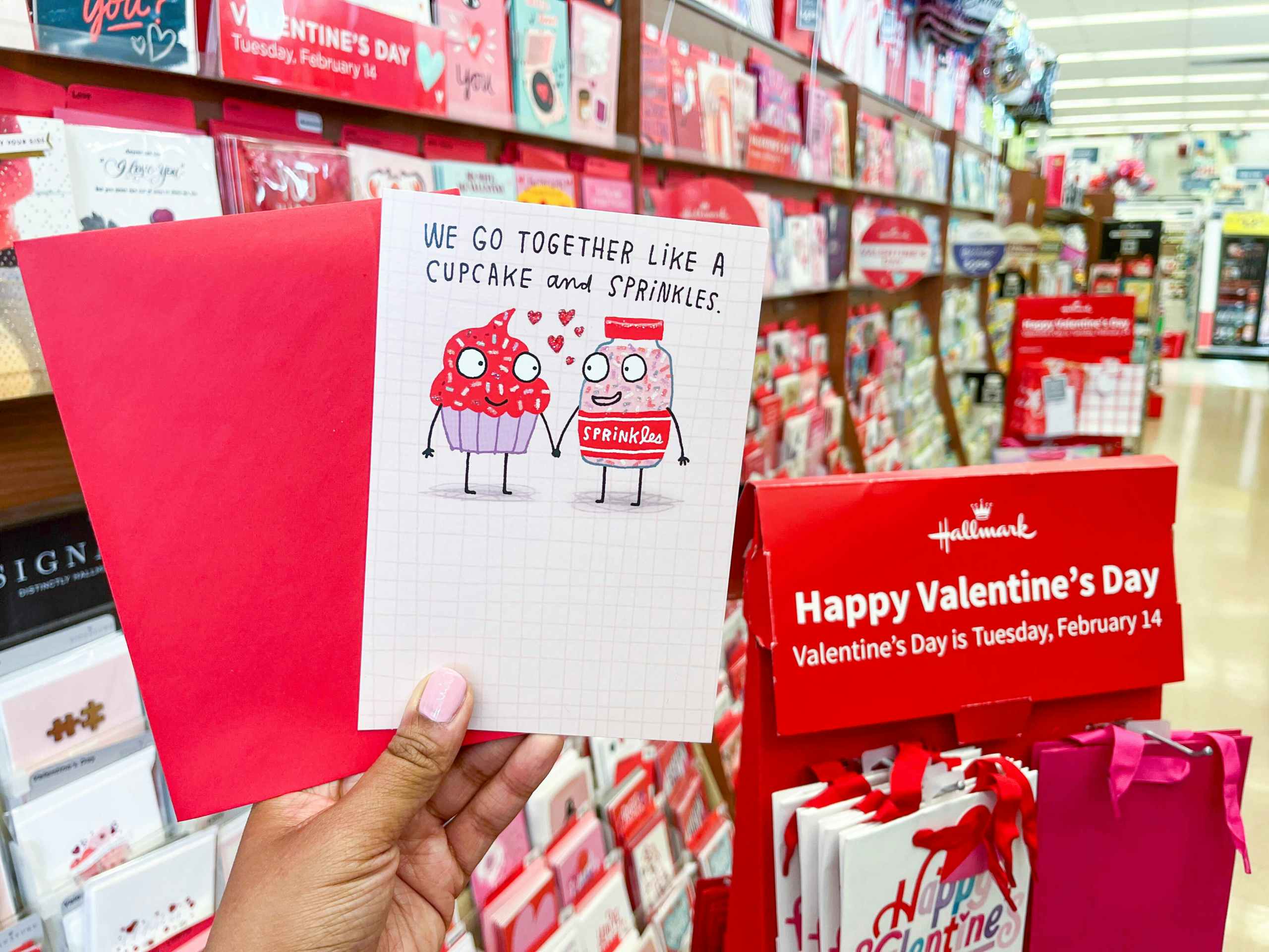 hand holding up a Hallmark Valentine's Day greeting card in front of Valentine's day card display