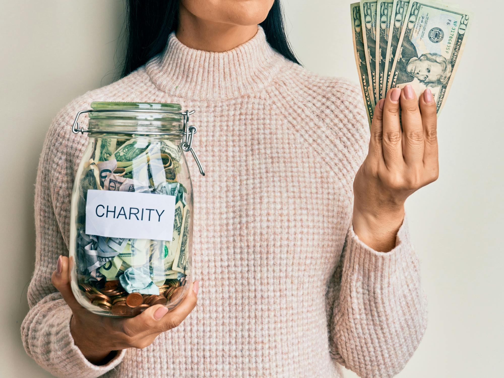 a person holding a charity jar and money smiling looking to the side