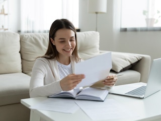 person smiling at a piece of mail sitting in their living room