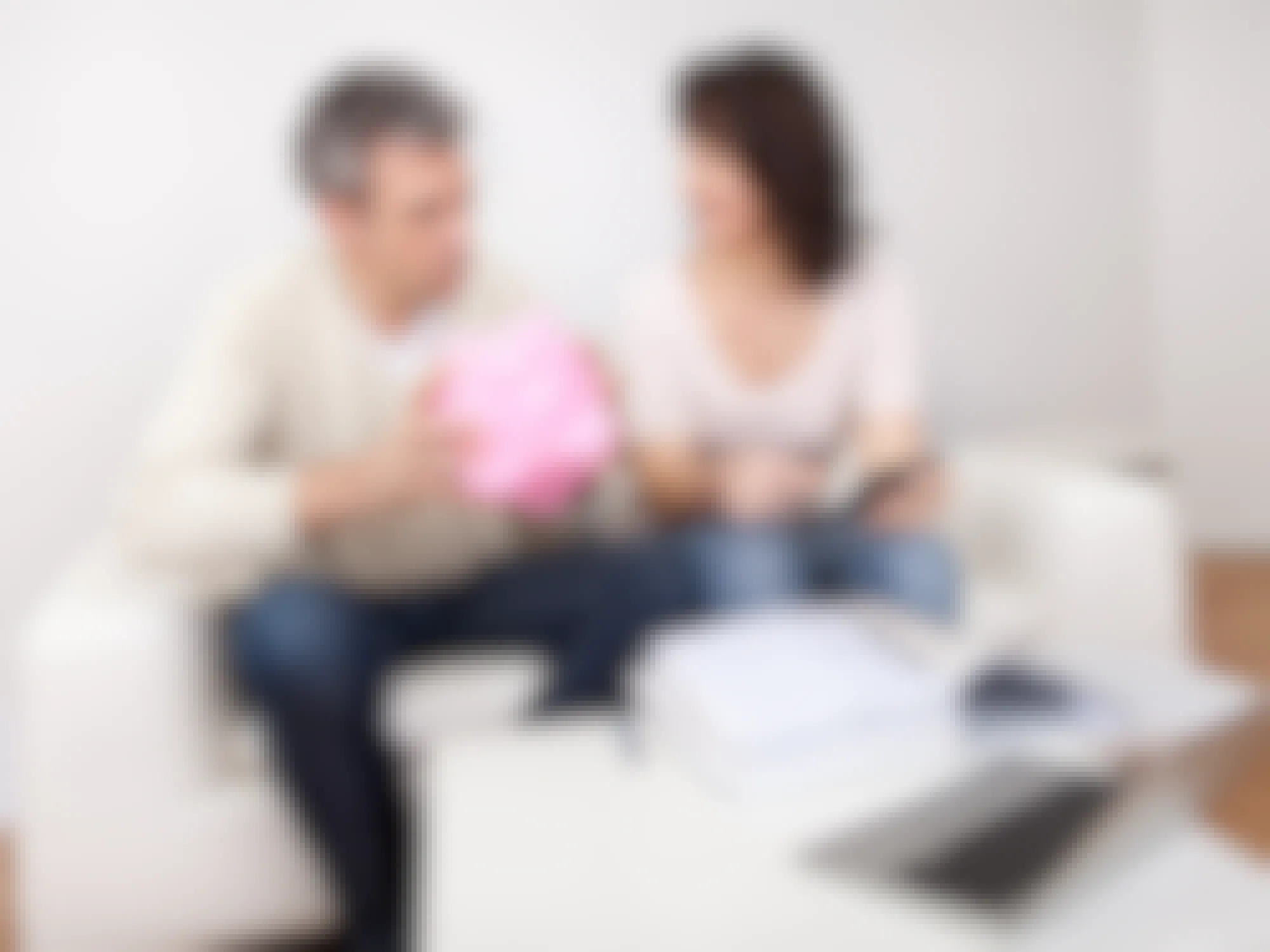 two people sitting on a couch one is talking and the other is holding a pink piggy bank