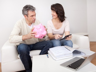 two people sitting on a couch one is talking and the other is holding a pink piggy bank