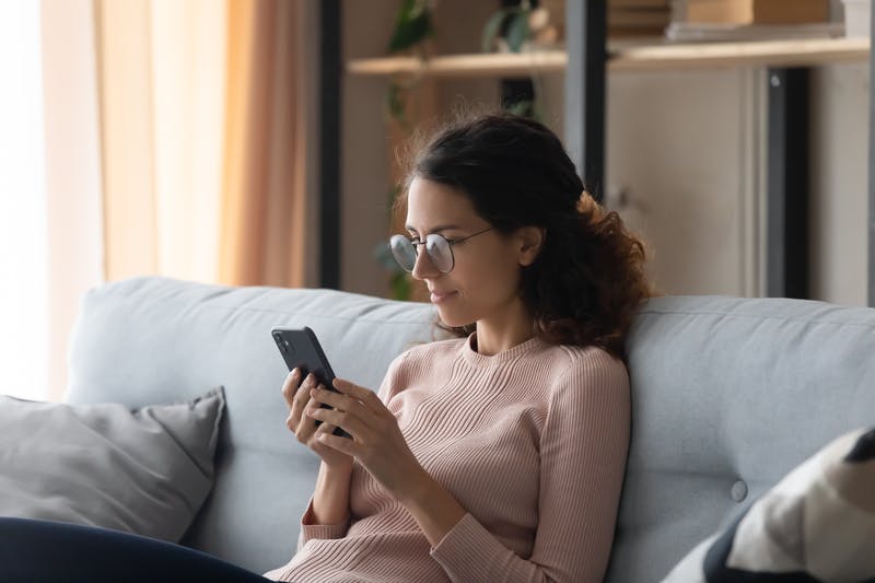 a woman sitting on a couch looking at her cellphone 