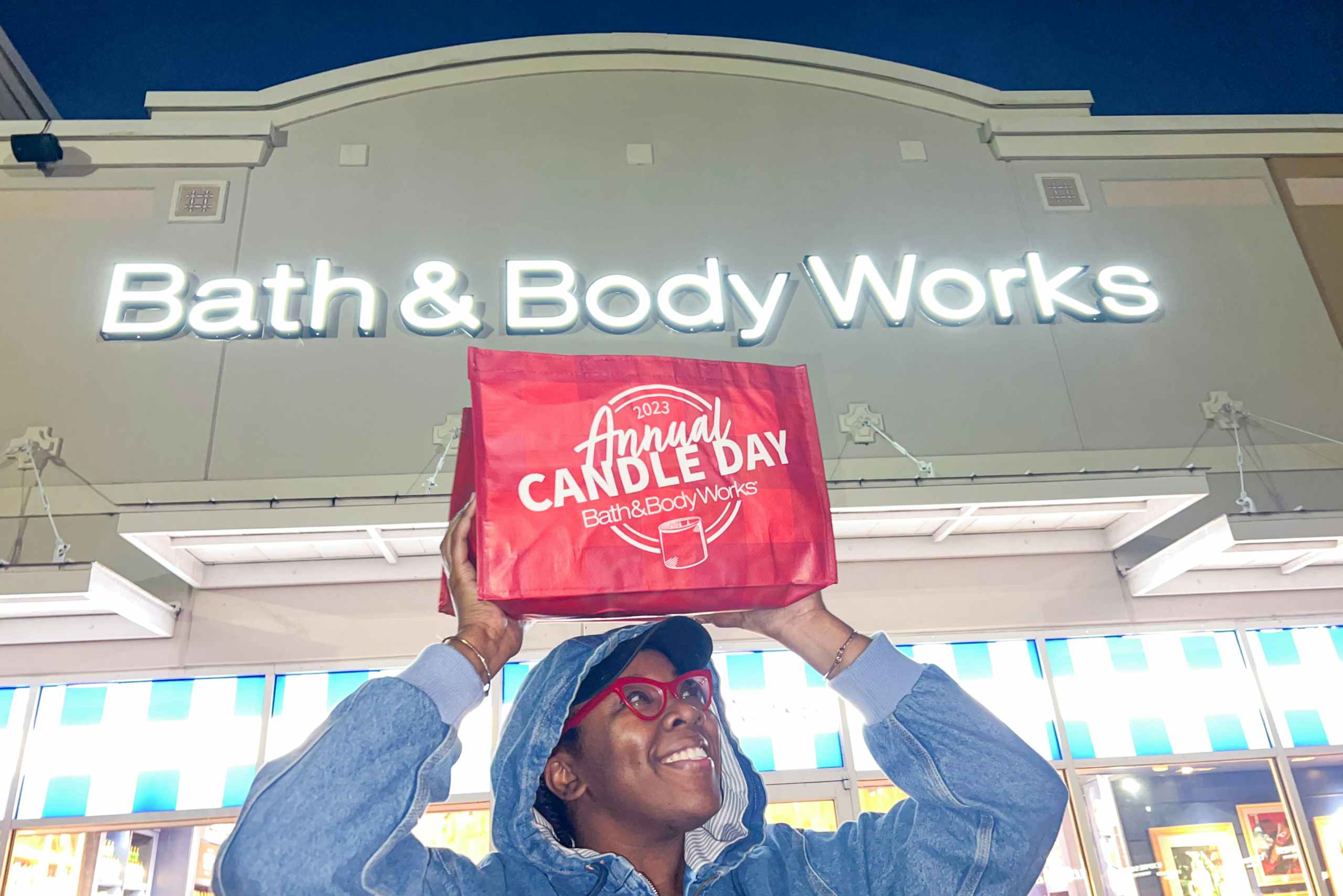 Person holding up a large Bath and body works candle day bag infront of store