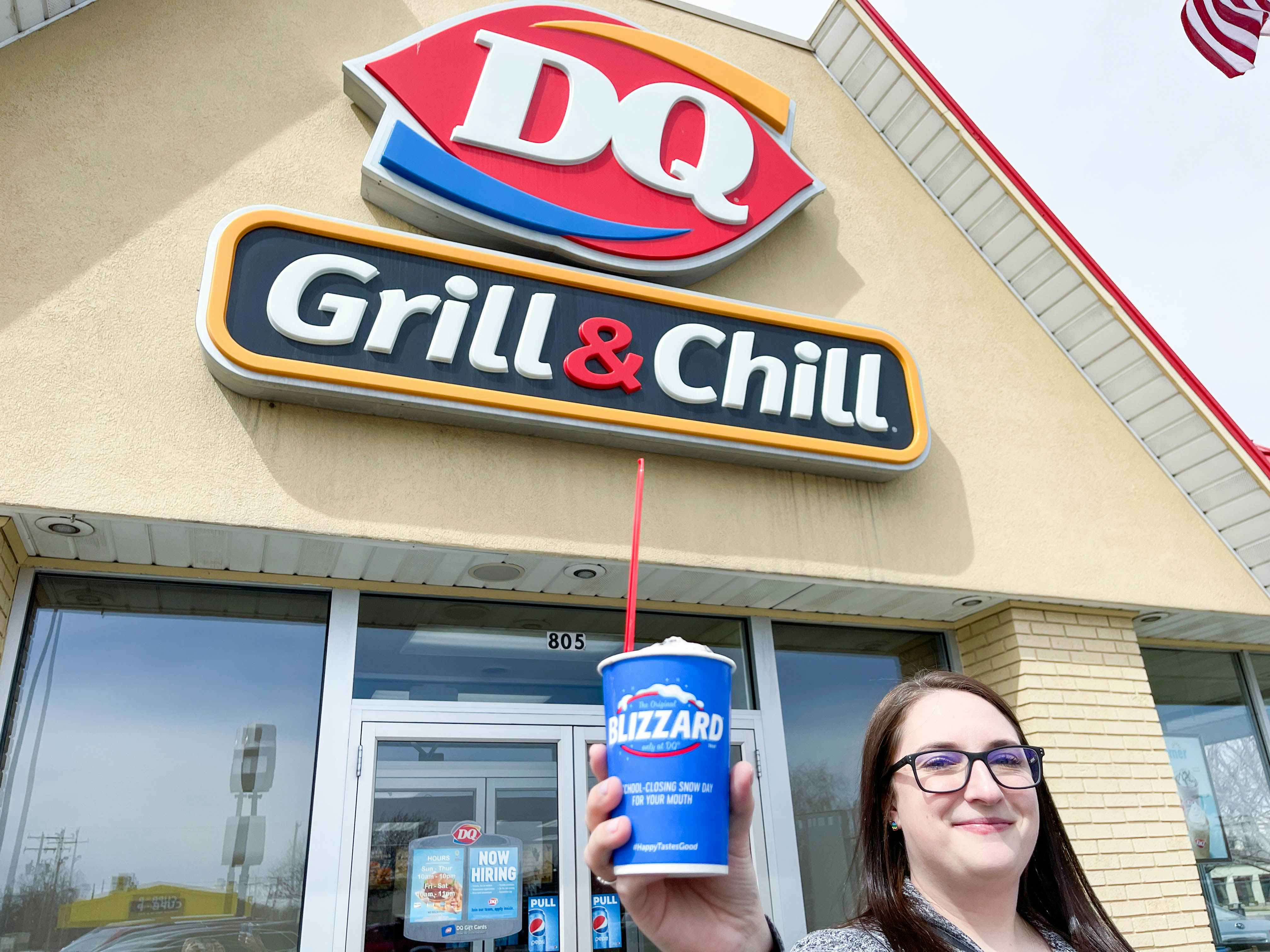 a person standing in front of the dairy queen sign holding up a blizzard