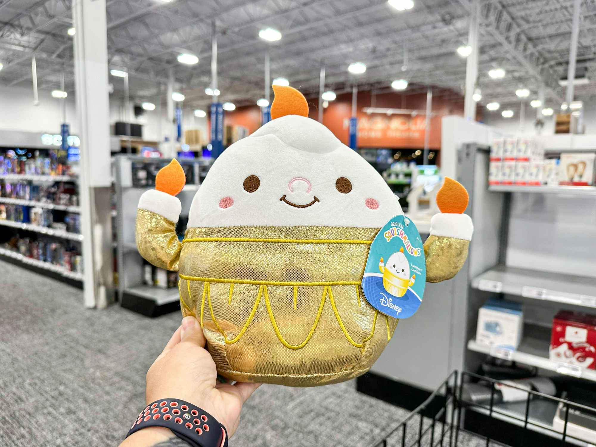 a person holding up a disney squishmallow in best buy 