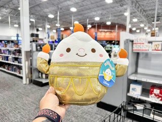 a person holding up a disney squishmallow in best buy