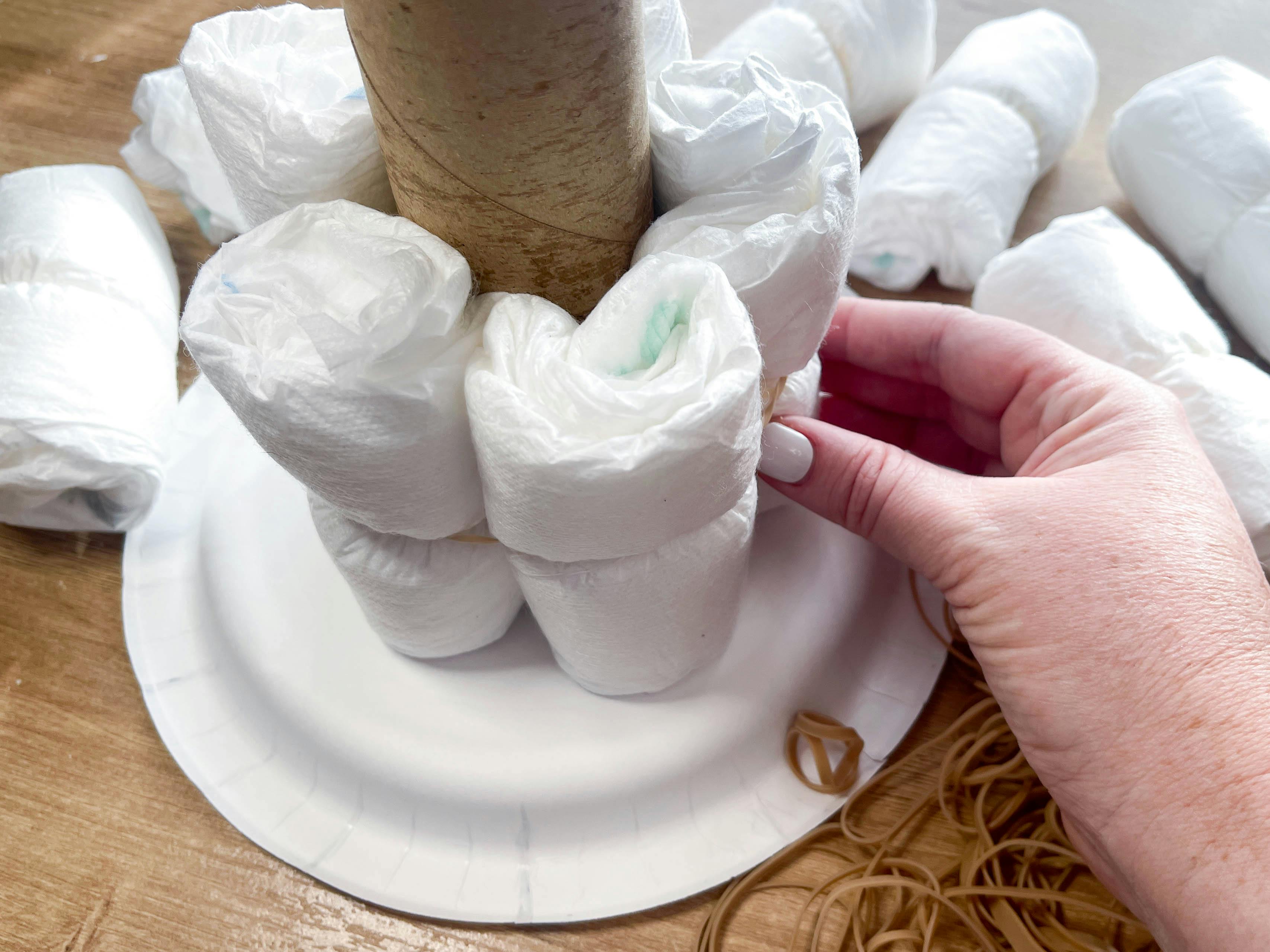 a person adding rolled up diapers on a base of a diy diaper cake structure 