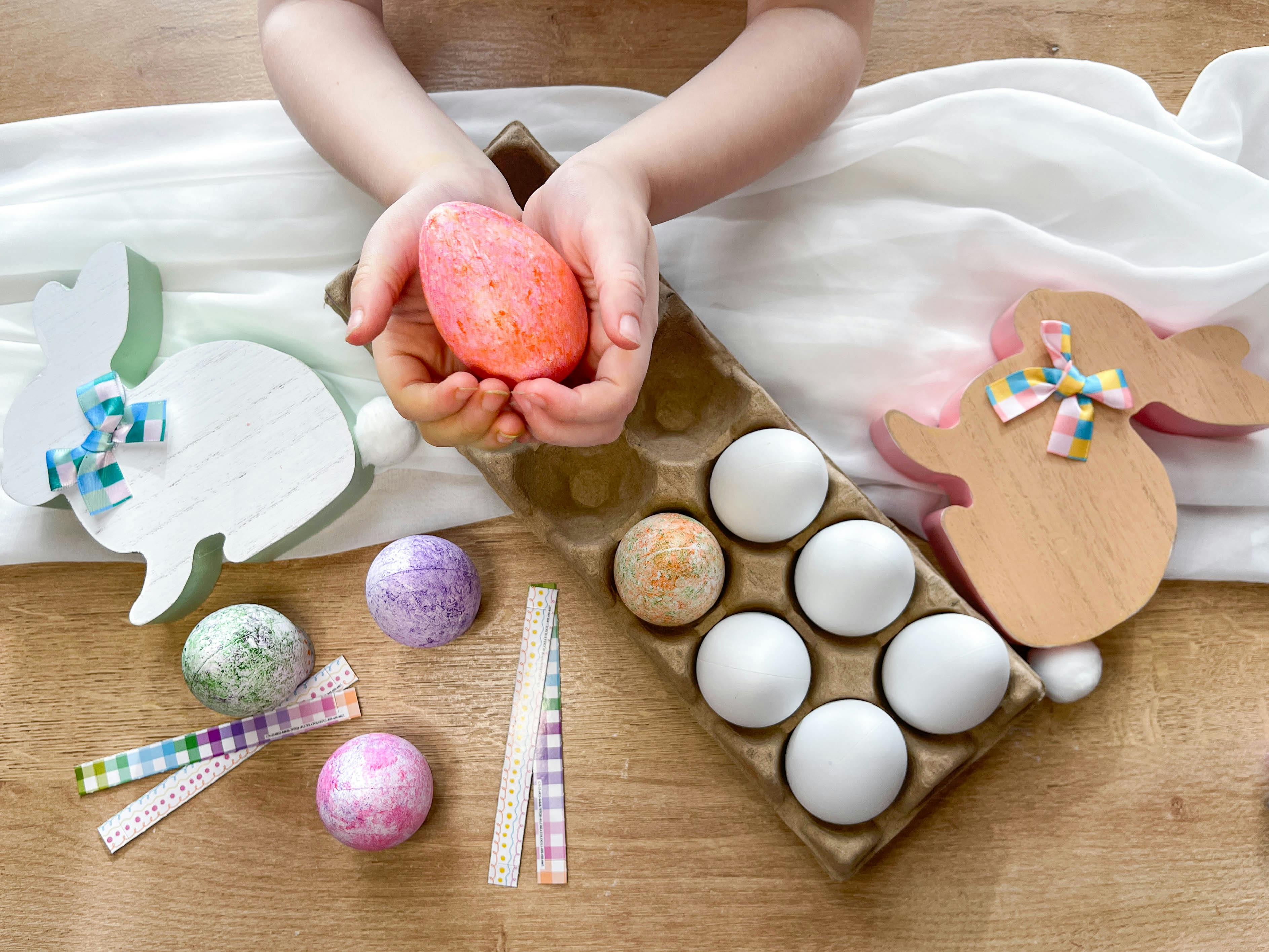 a kid holding a dyed egg near other plastic eggs and easter decor