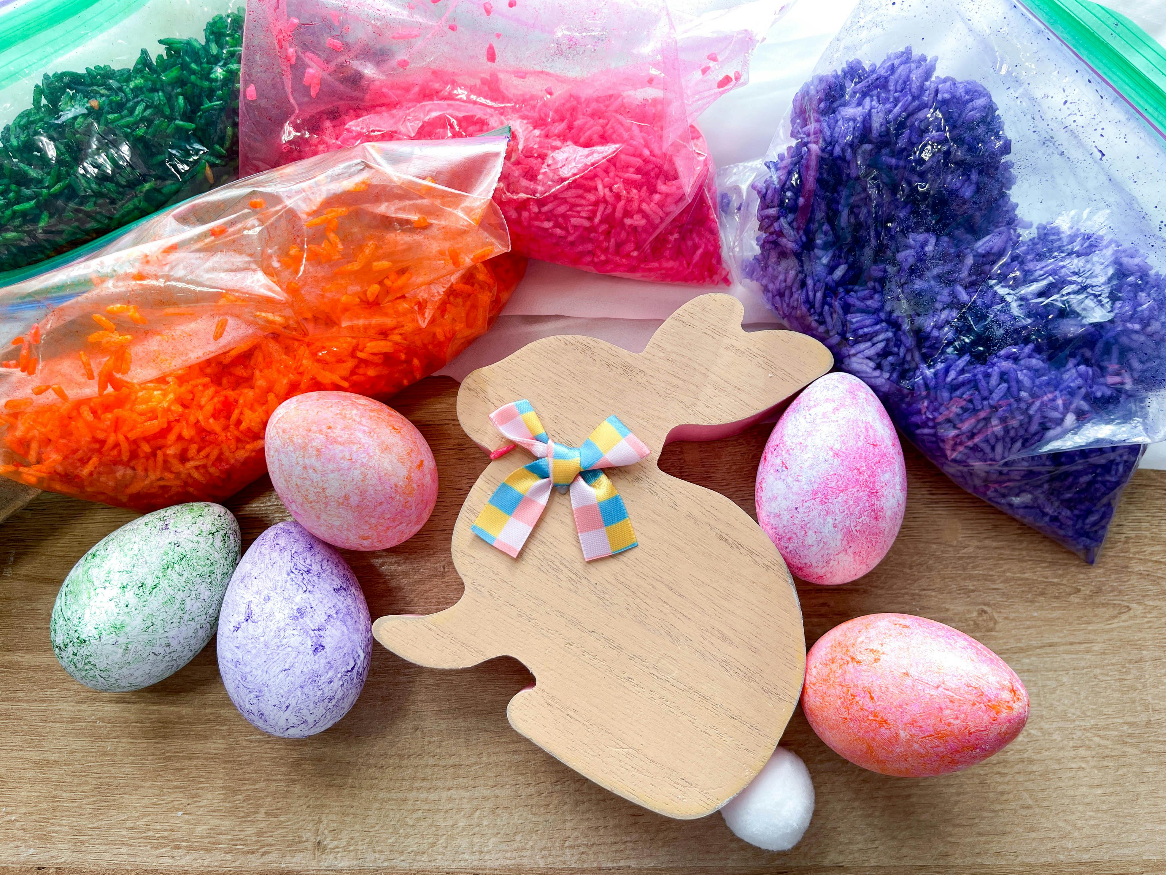 Dyed plastic eggs next to easter decor and bags of colored rice on a table