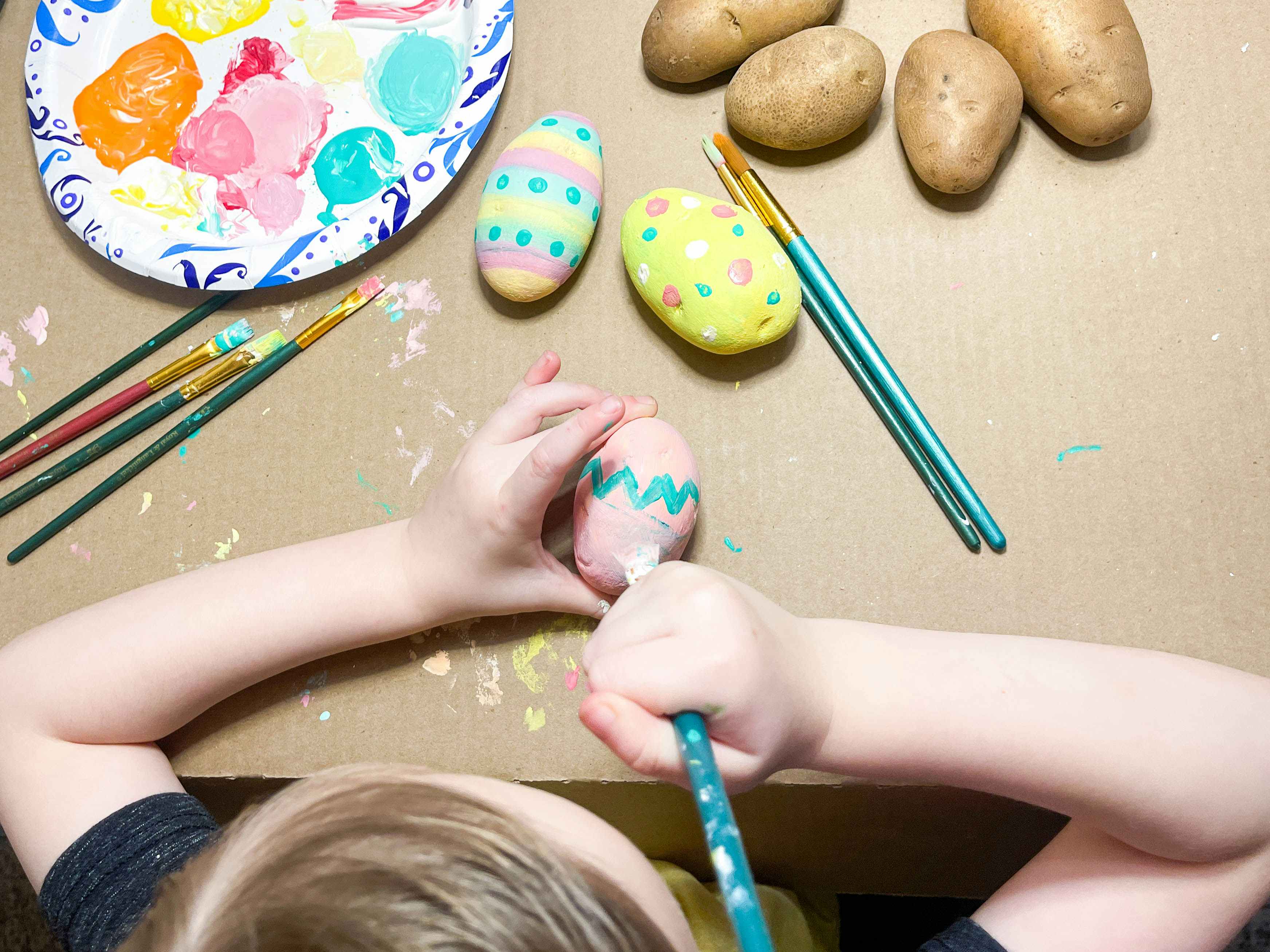 a little kid painting a potato to look like an easter egg