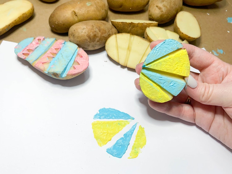 a person holding a painted potato stamp next to the stamp imprint on paper