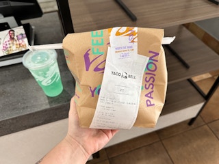 Someone holding up their Taco Bell order in a bag by the counter inside Taco Bell