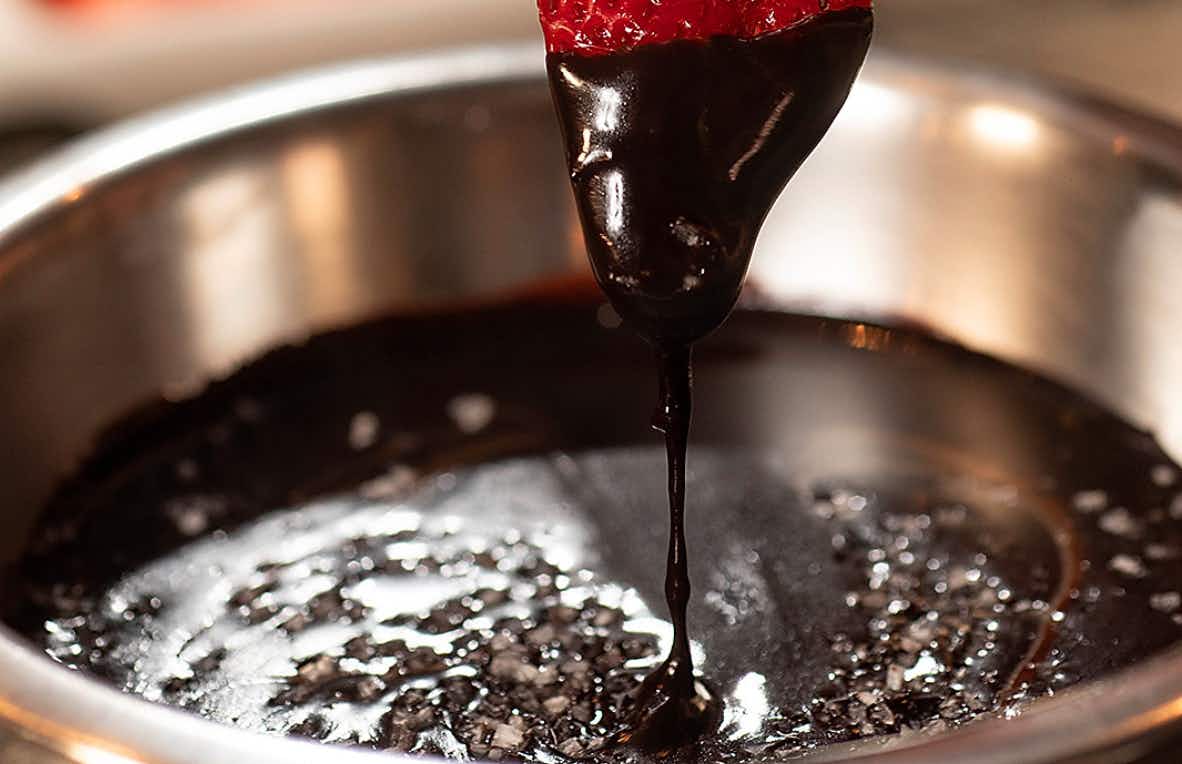 a strawberry being dipped into chocolate fonude from the melting pot.