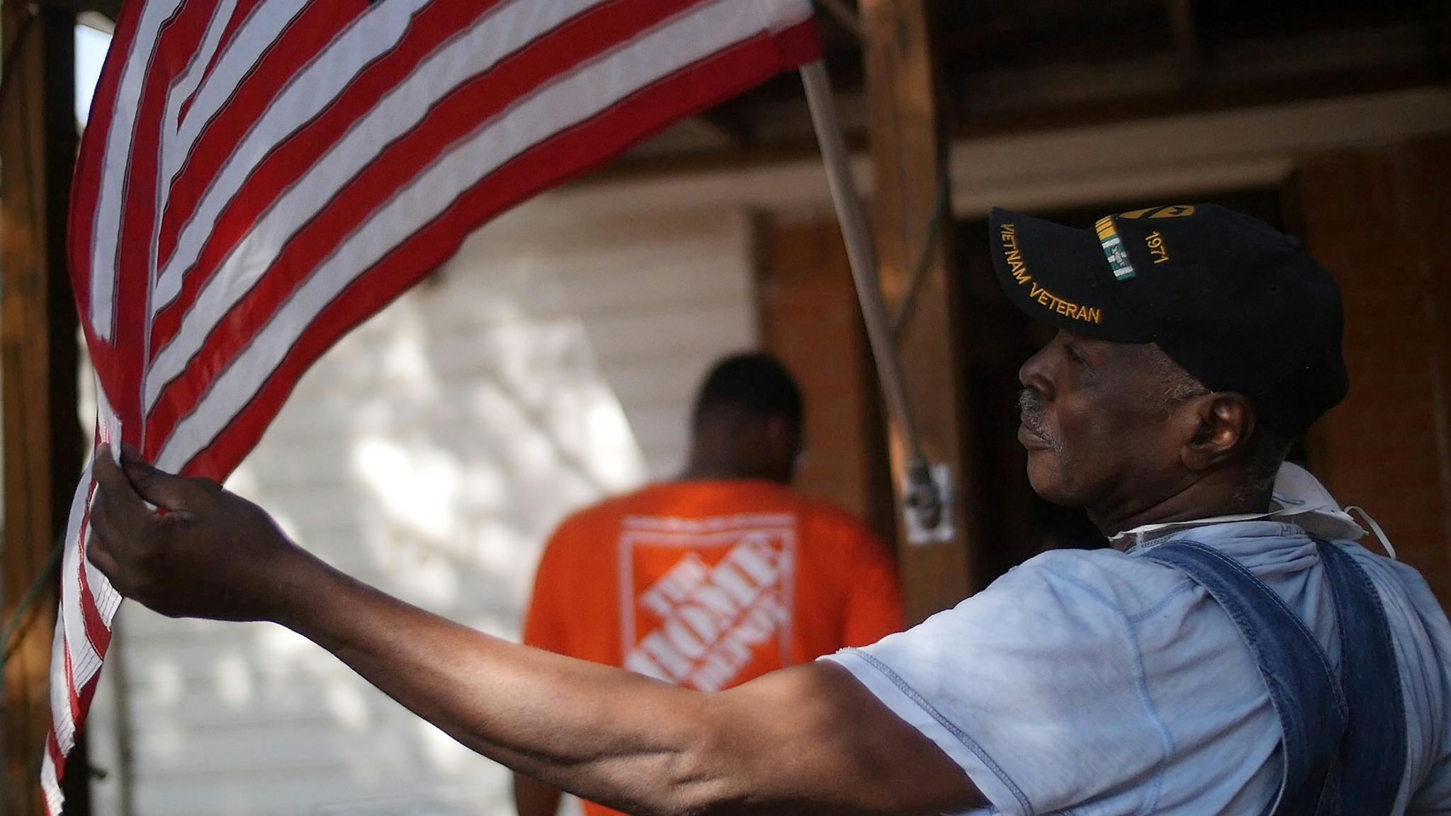 A veteran holding an American flag in front of someone wearing a Home Depot shirt