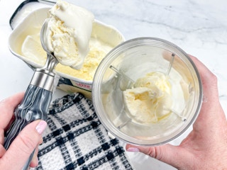a person scooping vanilla ice cream to put into a blender cup